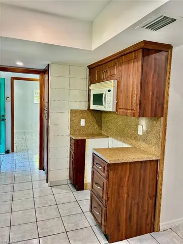 Kitchen with light tile patterned floors, decorative backsplash, white microwave, and brown cabinetry