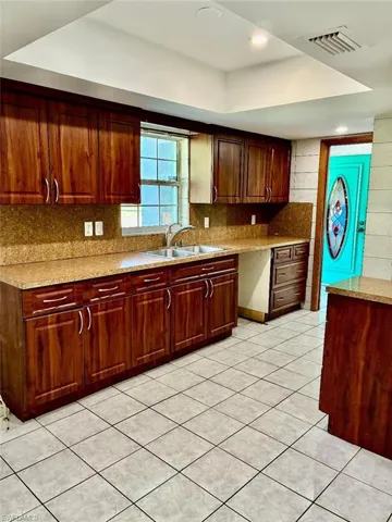 Kitchen with a raised ceiling, light tile patterned floors, tasteful backsplash, and light stone countertops