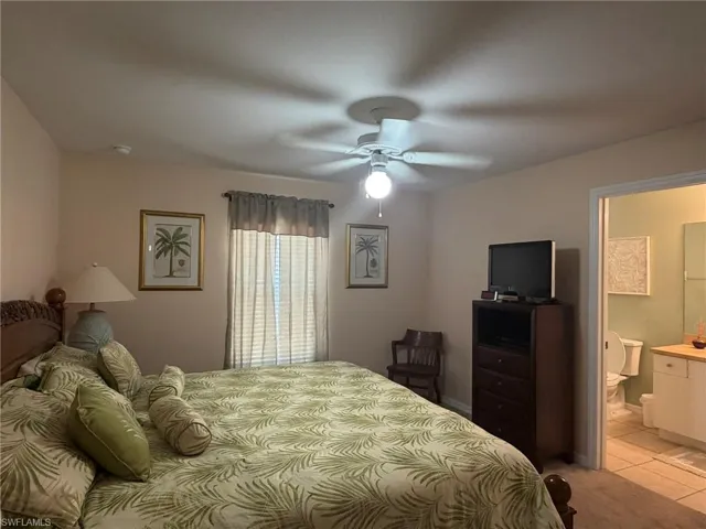 Bedroom featuring ceiling fan, light tile patterned floors, and ensuite bathroom
