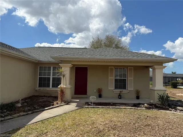 View of exterior entry featuring roof with shingles, stucco siding, a porch, and a lawn