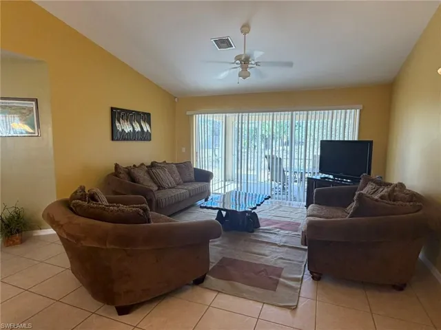 Living room with a ceiling fan, lofted ceiling, and light tile patterned flooring