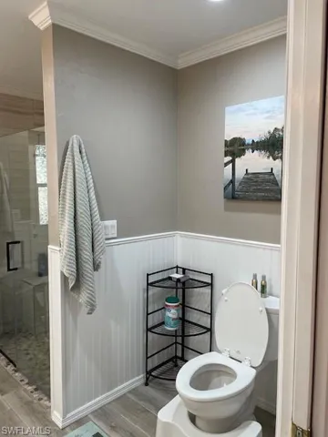 Bathroom with hardwood / wood-style floors, a shower with shower door, toilet, and ornamental molding
