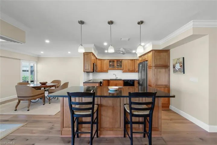 Open-concept kitchen featuring wood-finish cabinetry, black appliances, and a dark stone countertop island with pendant lighting
