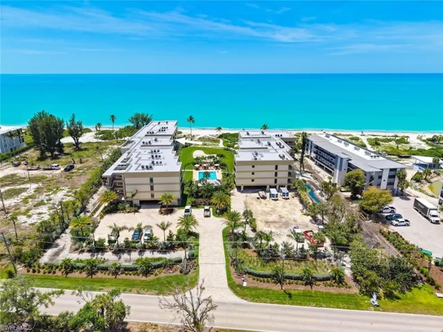 Coastal condominium complex with direct beach access, featuring multiple buildings, a central swimming pool, and dedicated parking areas
