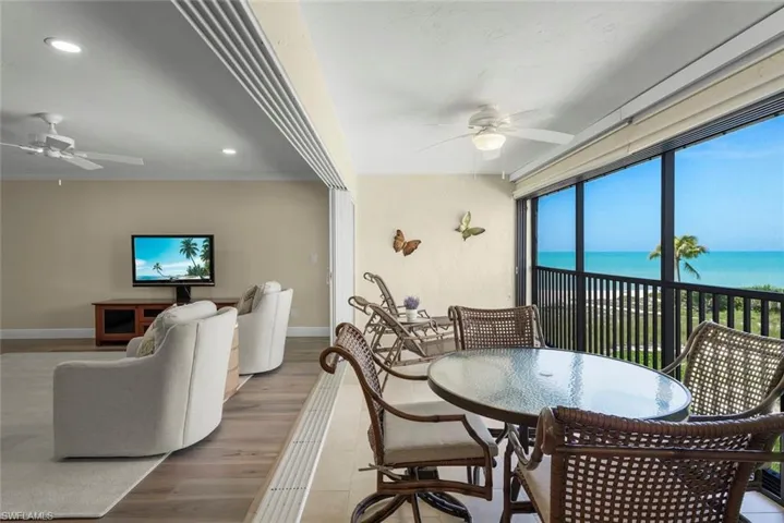 Expansive screened balcony featuring a glass-top table, wicker seating, and direct water views