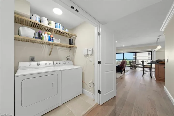 Dedicated laundry area featuring a white washer and dryer pair, light-toned tile flooring, and two wall-mounted wooden shelves