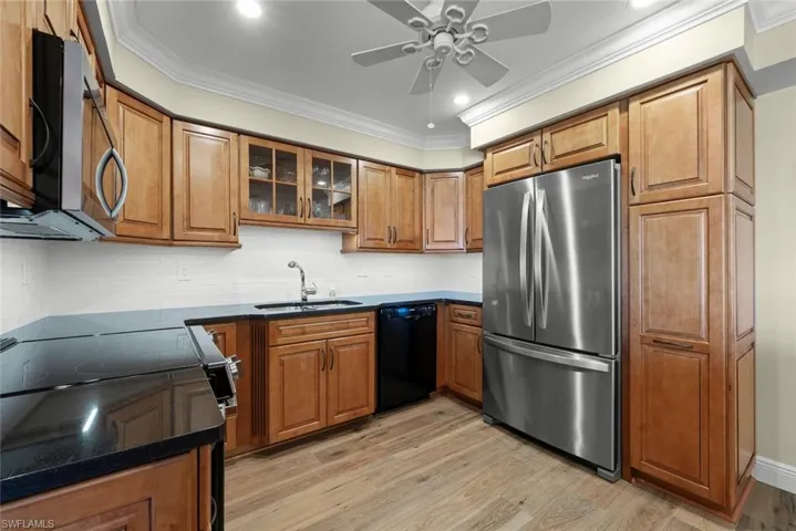 Kitchen featuring wood cabinetry, stainless steel appliances, black countertops, and a white subway tile backsplash