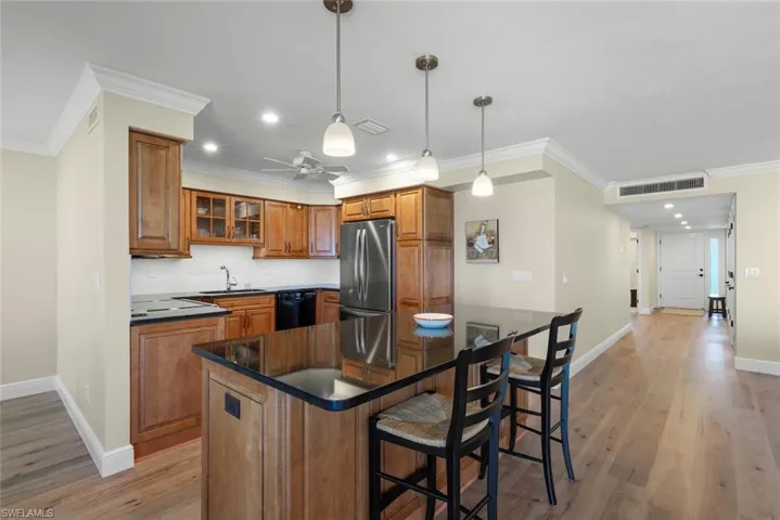 Kitchen featuring wood cabinetry, dark countertops, stainless steel refrigerator, white tile backsplash, and wood-finish flooring