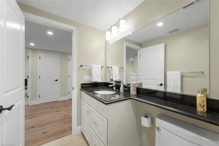 Bathroom featuring a white vanity with panel cabinetry, a dark countertop, an integrated sink, and an expansive wall-mounted mirror