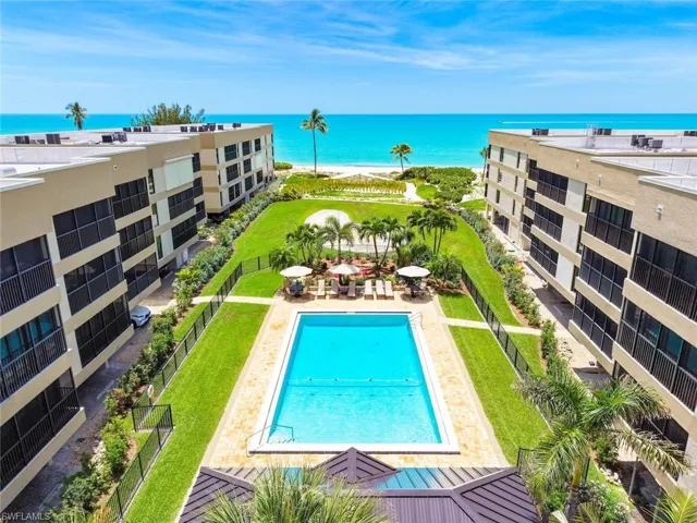 Beachfront property featuring a rectangular swimming pool with surrounding patio, lush green lawns, and mature palm trees