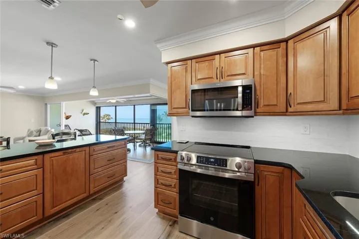 Kitchen featuring wood-finish cabinetry, stainless steel appliances, black countertops, and a white subway tile backsplash
