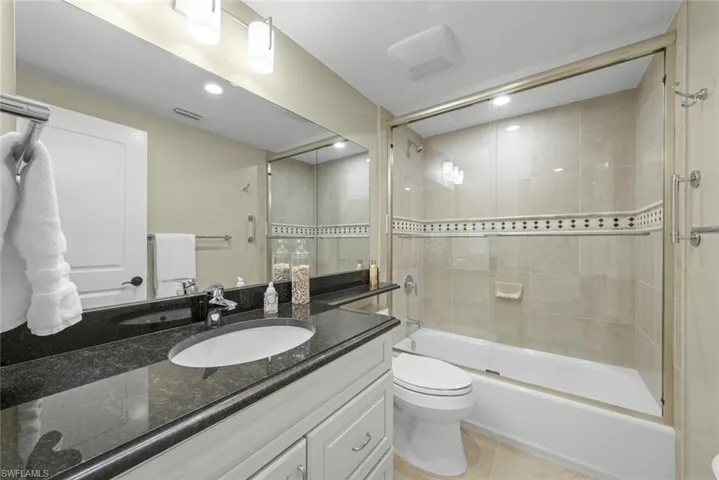 Full bathroom featuring a single vanity with a dark countertop, an undermount sink, and light-toned cabinetry