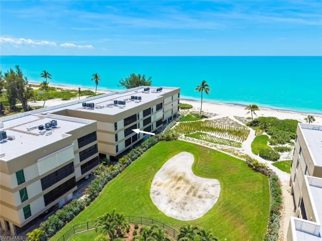 Beachfront property featuring a sand-colored exterior, multiple balconies, a manicured lawn, and lush landscaping