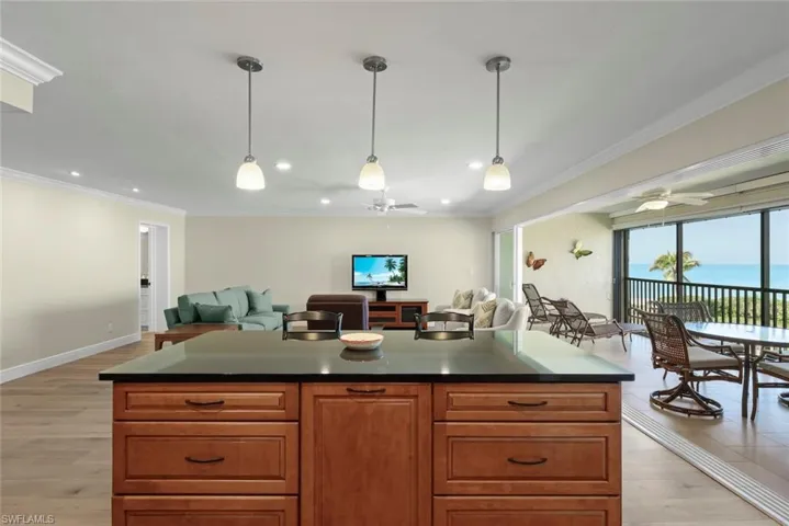 Kitchen island with dark countertop, wood-finish cabinetry, and pendant lighting