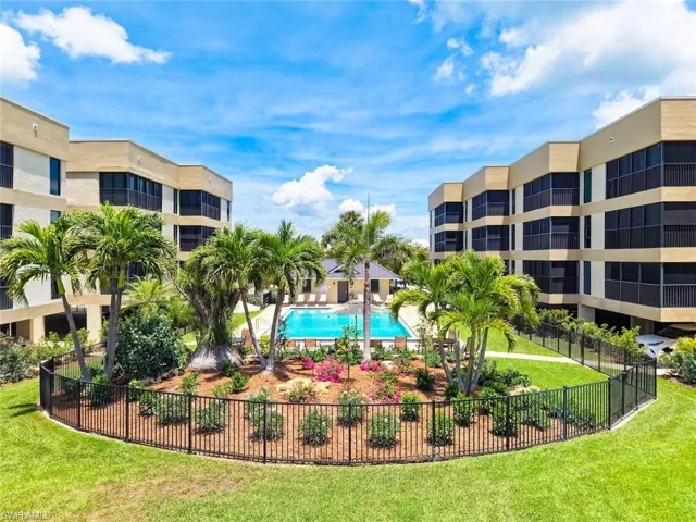 Central outdoor swimming pool with surrounding lounge chairs, bordered by lush tropical landscaping and mature palm trees