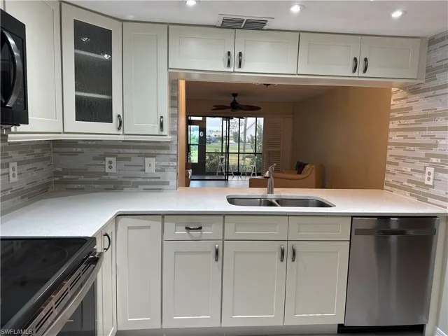 Kitchen featuring decorative backsplash, electric range, stainless steel dishwasher, white cabinets, and sink