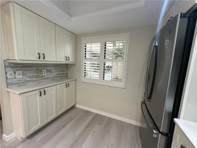 Kitchen featuring tasteful backsplash, a raised ceiling, ornamental molding, white cabinets, and stainless steel fridge