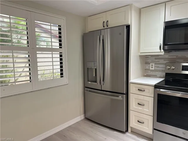 Kitchen with white cabinets, appliances with stainless steel finishes, light wood-type flooring, and tasteful backsplash