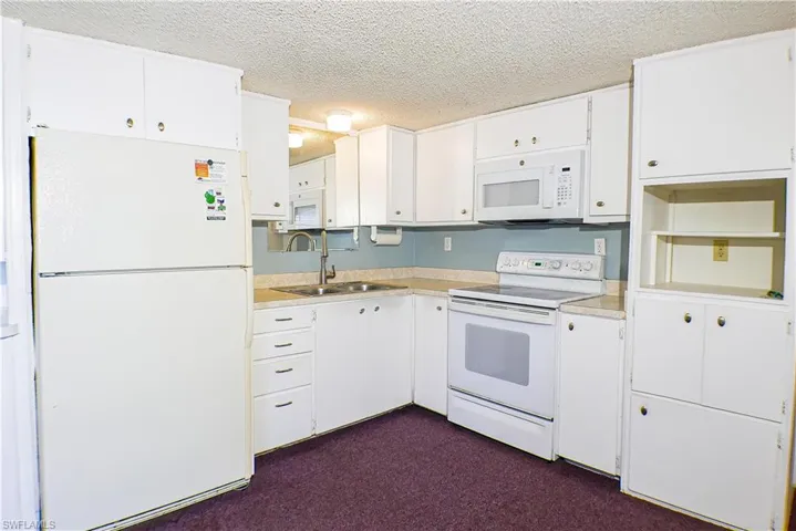 Kitchen featuring white appliances, sink, dark colored carpet, and white cabinets