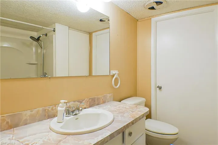 Bathroom featuring a shower, vanity, toilet, and a textured ceiling