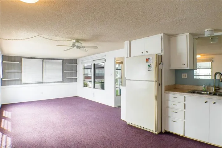 Kitchen featuring a textured ceiling, sink, ceiling fan, white refrigerator, and white cabinets