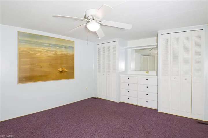 Unfurnished bedroom with dark carpet, ceiling fan, and multiple closets