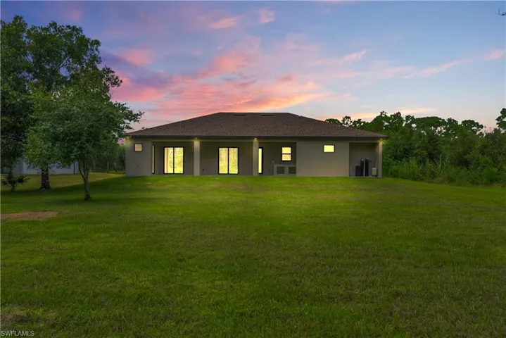 Rear view of house featuring a lawn, stucco siding, and a patio