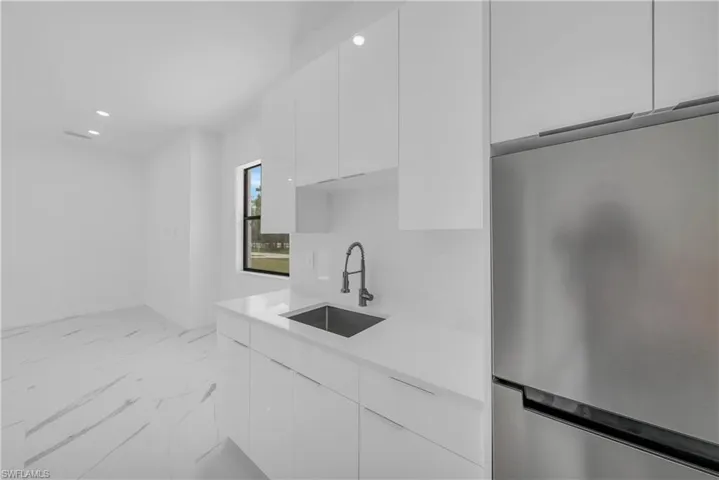 Kitchen featuring freestanding refrigerator, modern cabinets, white cabinetry, recessed lighting, and light stone countertops