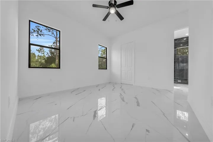 Unfurnished bedroom with marble finish floors, ceiling fan, and ensuite bath