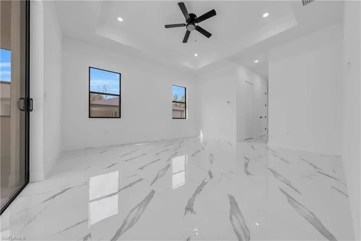 Spare room featuring a raised ceiling, recessed lighting, light marble finish floors, and a ceiling fan