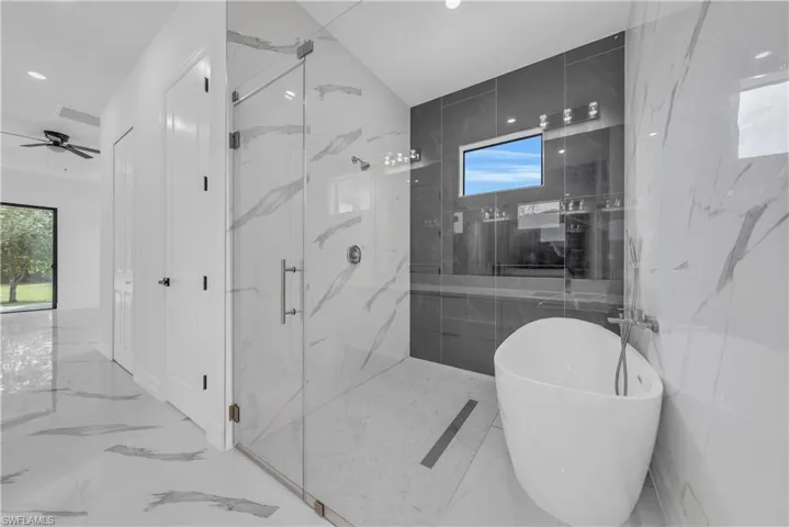 Bathroom with marble tiled flooring, a soaking tub, a marble finish shower, stone wall, and recessed lighting