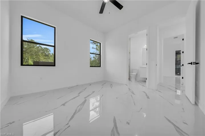Unfurnished bedroom with light marble finish floors, ceiling fan, and ensuite bath