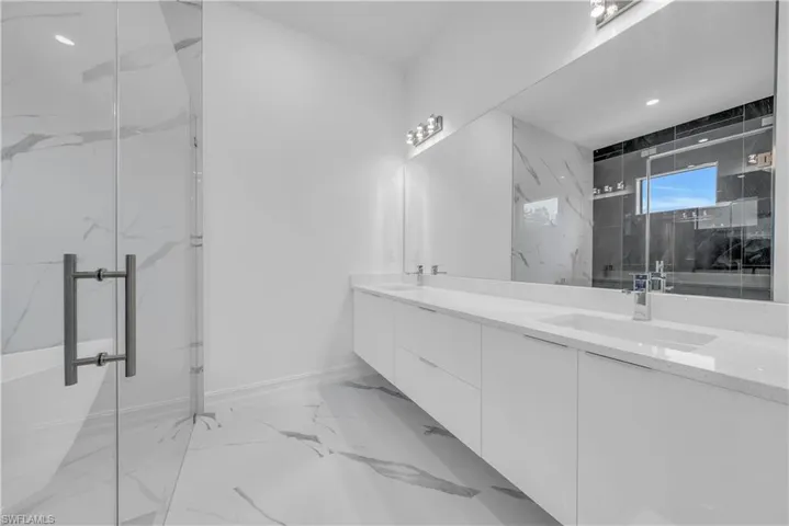 Bathroom with light marble finish flooring, double vanity, and a marble finish shower