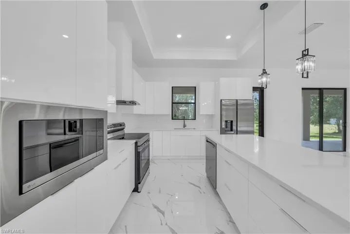 Kitchen with modern cabinets, white cabinets, appliances with stainless steel finishes, decorative light fixtures, and a raised ceiling