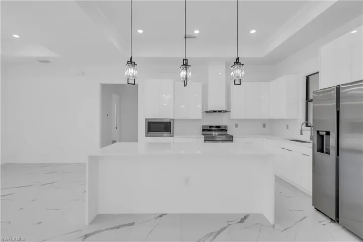 Kitchen featuring appliances with stainless steel finishes, decorative light fixtures, recessed lighting, a raised ceiling, and white cabinets