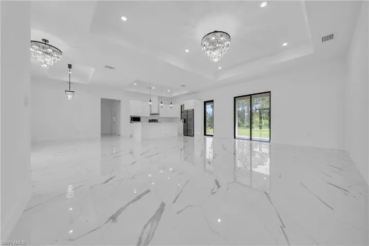 Unfurnished living room featuring a chandelier, a raised ceiling, light marble finish floors, and recessed lighting
