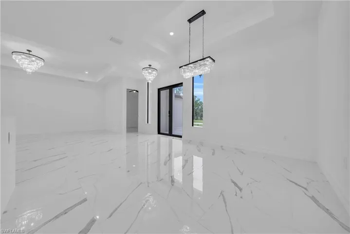 Unfurnished room featuring a raised ceiling, a chandelier, light marble finish floors, and recessed lighting