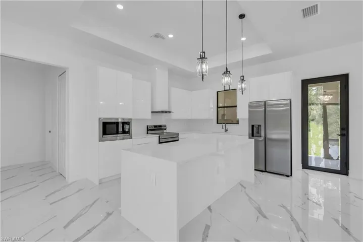 Kitchen featuring a raised ceiling, a center island, modern cabinets, appliances with stainless steel finishes, and white cabinetry