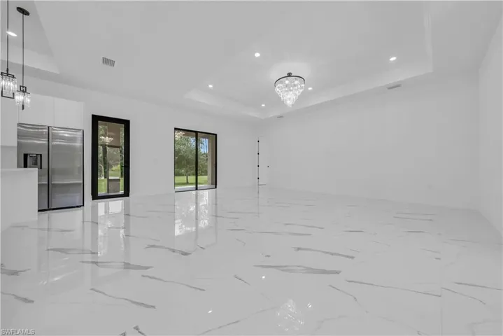 Empty room with a chandelier, a tray ceiling, light marble finish floors, and recessed lighting