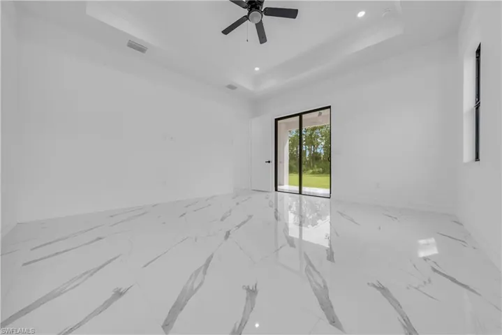 Empty room with a raised ceiling, marble finish flooring, recessed lighting, and a ceiling fan
