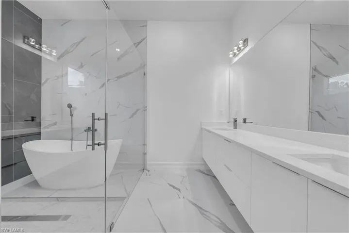Bathroom featuring double vanity, a soaking tub, and light marble finish floors