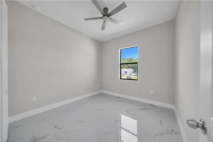 Room with light gray walls, large window, ceiling fan, and white baseboards