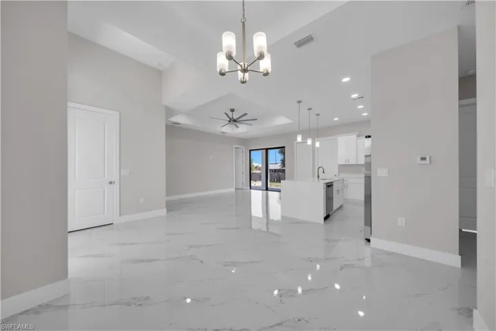 Spacious living area featuring polished tile flooring, a modern chandelier, and vaulted ceilings