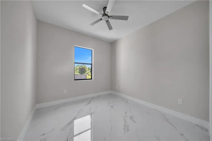 Spacious room featuring large format tile flooring, a window with a black frame, a ceiling fan with integrated lighting, and neutral wall paint