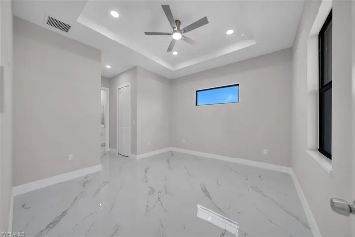 Spacious interior featuring marble-look tile flooring, a tray ceiling with recessed lighting, and a modern ceiling fan