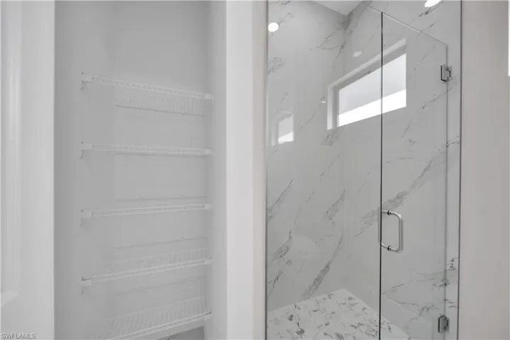 Walk-in shower with clear glass enclosure and chrome hardware, featuring marble-look wall tile and a complementary tile floor