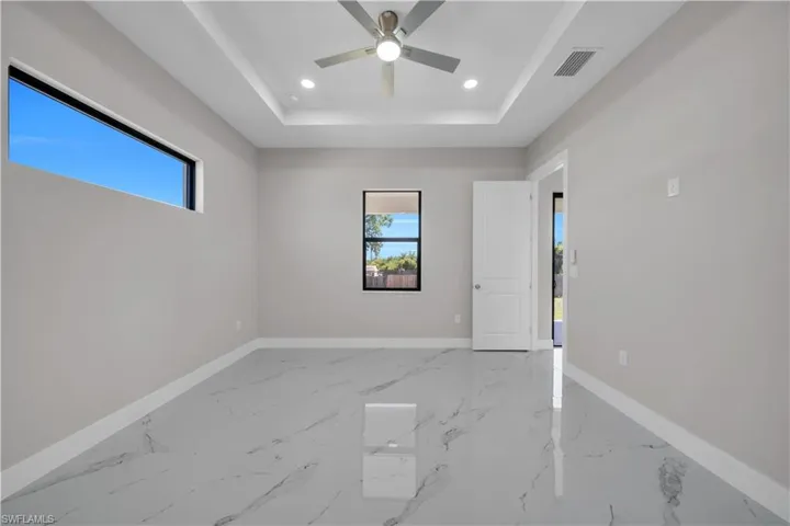 Spacious room featuring large format marble-look tile flooring, a tray ceiling with recessed lighting, and a ceiling fan