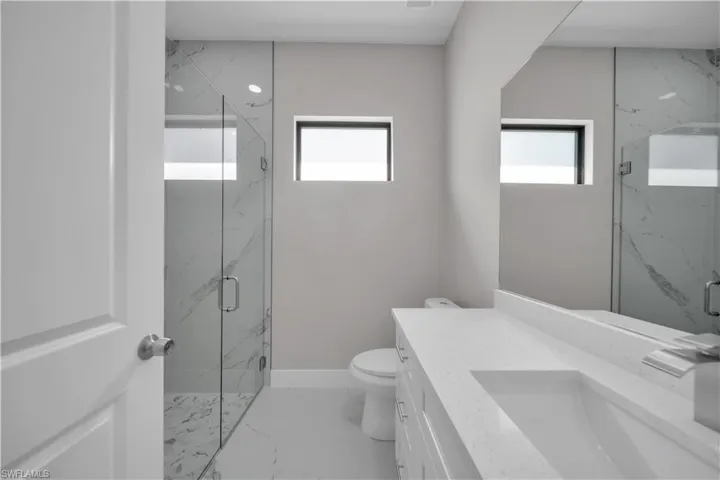 Contemporary bathroom featuring a frameless glass shower enclosure, a full-height vanity mirror, a single vanity with an integrated sink, and two horizontal windows