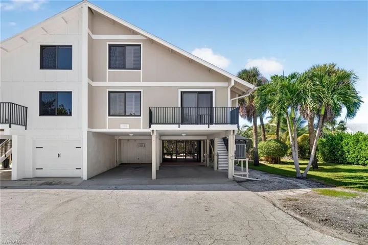 Multi-level exterior featuring a two-tone facade, elevated balcony with black metal railing, integrated ground-level garage, and covered parking area
