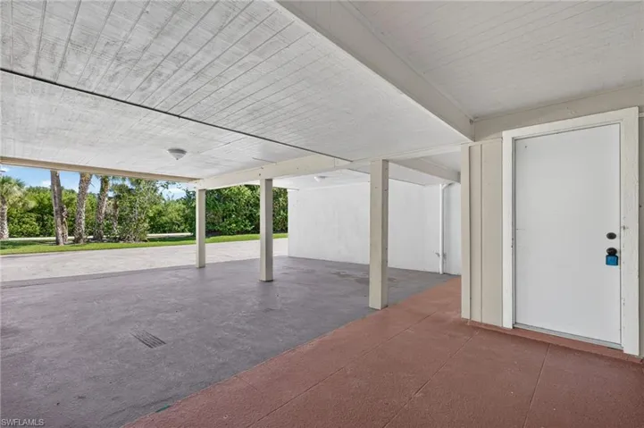 Covered carport with a concrete slab, supporting pillars, and a private exterior access door